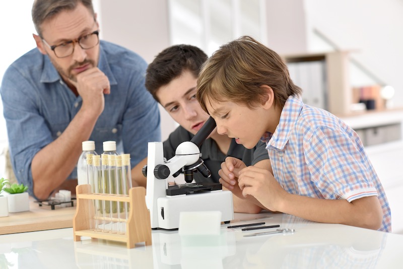 Familie mit Kindern am Mikroskop, Symbolbild für das Thema Bildung